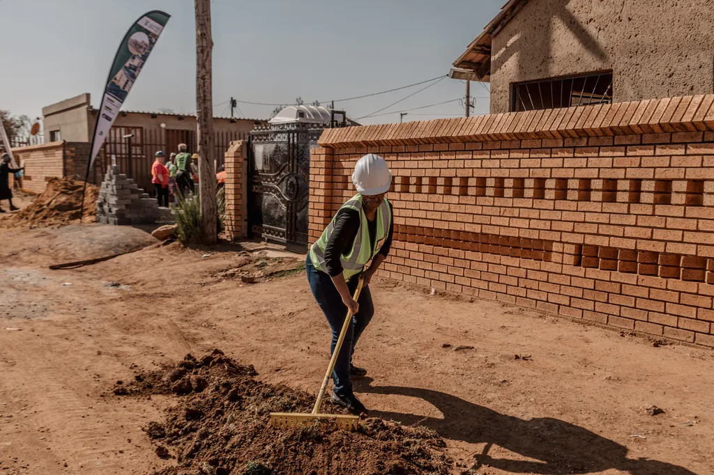 A team member digging a trench beside a face-brick wall