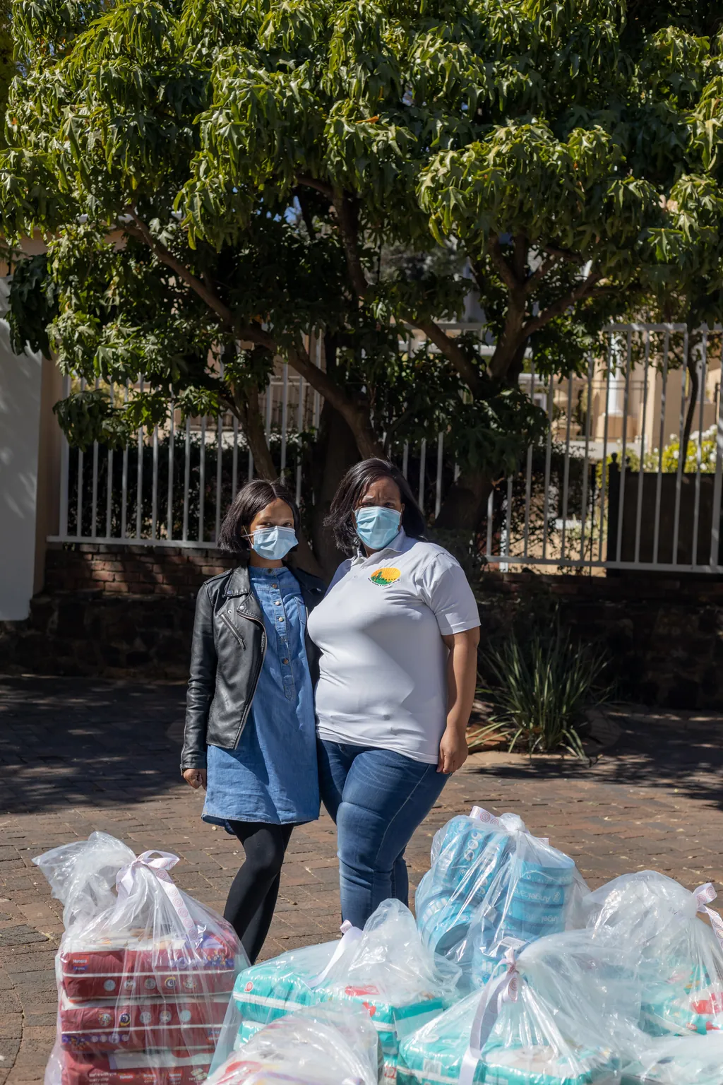 Two team members standing beside donated parcels under a tree at the gate