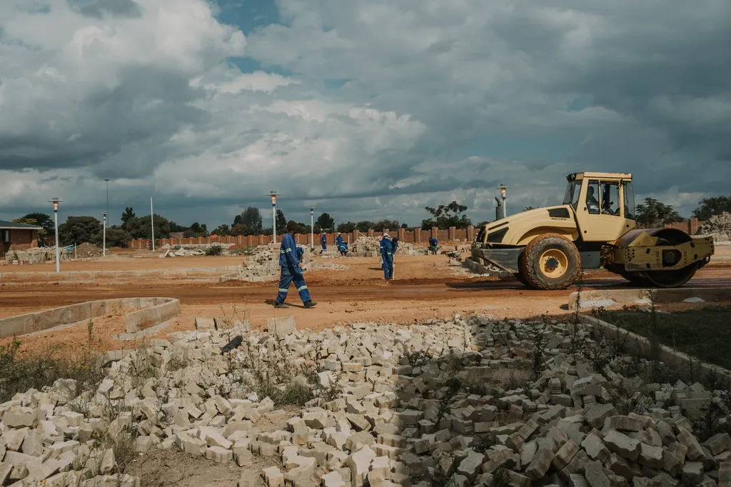 A road roller and workers in blue overalls preparing ground on a construction site